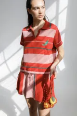 Remera polo tejida a rayas horizontales rojas y rosadas, con cuello clásico y bordado de ají verde.