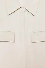 Camisa color beige de cuello solapa y manga corta. Tiene dos bolsillos delanteros con solapa y cierre frontal con botones.