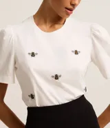 Blusa blanca de algodón con cuello redondo, mangas cortas abullonadas y bordados de abejas.