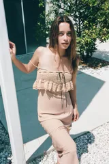 Vestido largo color beige, de escote recto y tirantes finos. Presenta bordados florales, aplicación de encaje y lazo satinado negro ajustable con lazada.
