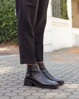 Botinetas de cuero negro con diseño de caña baja y puntera cuadrada. Presentan un panel trasero con textura tipo reptil y un taco bloque bajo de estilo moderno.