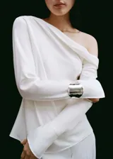 Blusa color blanco hueso de tejido satinado, con cuello drapeado y mangas largas con puños abiertos.