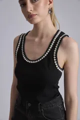 Remera negra ajustada al cuerpo, tipo musculosa, con escote redondo y ribetes en blanco con apliques de perlas en el contorno del cuello y las sisas.