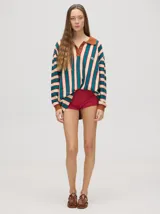 Chomba de corte oversize con cuello camisero, a rayas verticales en color marrón, lila y blanco. Tiene un logo bordado en el pecho y puños en color marrón.