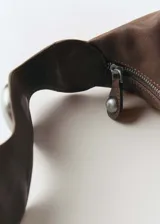Bolso marrón de cuero con asa de hombro y tachuelas decorativas plateadas.