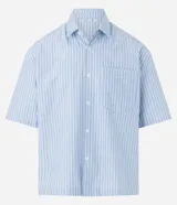 Camisa masculina oversized boxy de manga corta, confeccionada en tejido oxford a rayas verticales celestes y blancas. Cuenta con cuello inglés, abotonadura frontal y bolsillo de parche en el pecho.