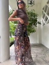 Falda larga de tela estampada con motivos florales en tonos marrones, negros y violetas. Tiene elástico en la cintura y corte acampanado.