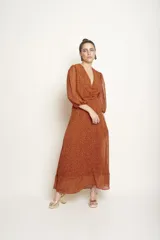 Vestido largo color naranja con estampado de manchas negras, escote en V, mangas largas abullonadas y corte evasé.