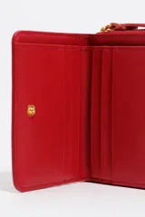 Billetera de cuero vacuno color rojo con estructura rígida y cierre de cremallera. Presenta un asa de tejido con el logo de la marca y el nombre de la firma en letras metálicas doradas en el frente.