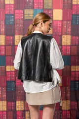 Chaleco corto negro de cuero con solapas y bolsillos frontales.