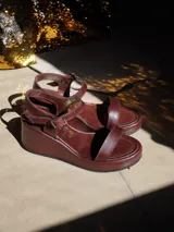 Sandalias de mujer con plataforma, tiras de cuero marrón y hebilla dorada. La plataforma es de color blanco con textura de piel de serpiente.