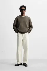 Pantalón de jean color crudo, corte amplio y tiro alto, con cinco bolsillos y cierre frontal con botones.