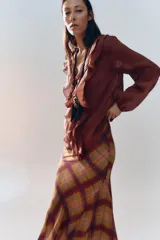 Camisa color crudo confeccionada en tejido con lyocell. Presenta escote en pico, mangas largas abullonadas con elástico en los puños, volantes frontales y cierre frontal con botones.