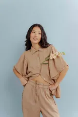 Camisa color beige de lino, con cuello clásico, mangas cortas abullonadas y cierre frontal con botones.