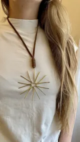 Collar con dije dorado en forma de sol y tiento de cuero marrón.