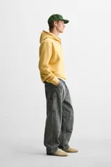 Pantalón color marrón con efecto lavado, corte relaxed fit, cinco bolsillos, aplicación de tira y bolsillo multifunción en perneras, cierre frontal con cremallera y botón.