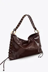 Bolso de hombro alargado color marrón oscuro, con detalle de pasados metálicos en los laterales y asa trenzada. Doble bolsillo interior con cremallera. Cierre mediante botón imantado.