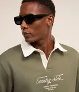 Sweater verde oliva de algodón y poliéster con cuello polo blanco, mangas largas y lettering bordado en el frente.