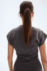 Vestido midi gris oscuro con finas rayas verticales blancas, escote drapeado tipo barco y mangas cortas caídas. Se ajusta a la cintura con un cinturón fino del mismo tejido y hebilla cuadrada.