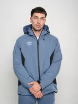 Campera corta de abrigo Umbro Crafted Pro, color negro con paneles laterales en gris. Presenta capucha con cordón ajustable, cierre frontal completo y logo de la marca bordado en el pecho.