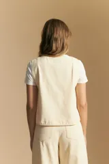 Chaleco negro de vestir con cuello solapa y cierre frontal de botones. Presenta costuras contrastantes blancas que definen el diseño y bolsillos delanteros. Se combina con una camisa blanca de manga larga.