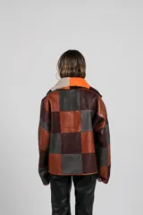 Buzo tipo anorak de cuero genuino, reversible, con diseño de parches en tonos marrones, naranjas y grises. Presenta cuello con solapas y cierre parcial frontal. El forro interior es de pelo sintético en tonos naranja y marrón oscuro.