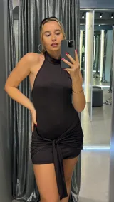 Vestido corto negro con cuello halter y falda drapeada con nudo.