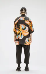 Camisa de manga corta negra con estampado de flores grandes en tonos amarillo, naranja y celeste. Corte oversize con canesú en la espalda.