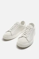 Zapatilla blanca de cordones fabricada en tejido transpirable de punto.