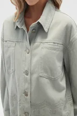 Campera de jean color crudo, de corte recto, con cuello clásico, cierre frontal con botones metálicos, dos bolsillos con solapa en el pecho y bajo con detalle de bordado calado.