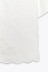 Camisa blanca de manga corta con escote en pico y cierre frontal con lazadas. Presenta bordados florales a tono.