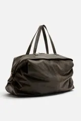 Bolso de viaje marrón oscuro fabricado en piel con acabado craquelado. Tiene un compartimento principal con cierre de cremallera, un bolsillo plano interior con cremallera y dos bolsillos frontales con botón a presión. Cuenta con asas de mano de piel y asa de hombro removible y ajustable.