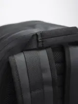 Mochila negra con cierre superior y bolsillo frontal con cierre. Tiene dos bolsillos laterales con cierre y un pequeño logo cuadrado en la parte inferior.