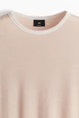 Remera color rosa claro de corte regular fit, con cuello redondo y mangas cortas. Presenta ribete en color gris claro en cuello y mangas.