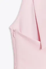 Top color rosa pálido, con cuello halter y escote en pico. Presenta un lazo en la espalda y cierre lateral con cremallera oculta.