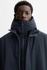 Parka azul marino de tejido técnico repelente al agua, corte regular fit, interior acolchado, cuello alto con capucha, mangas largas con puños de rib, cuello interior desmontable con cremallera, bolsillos de vivo en cadera y bolsillo interior. Cierre frontal con cremallera oculta por solapa con botones a presión.
