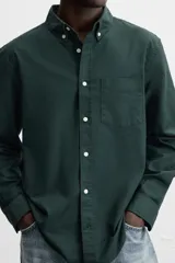 Camisa azul marino de corte regular fit, confeccionada en tejido de algodón Oxford. Tiene cuello abotonado, manga larga con puños abotonados, bolsillo de parche en el pecho y cierre frontal con botones.