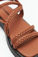 Sandalias color beige con plataforma negra, tiras trenzadas y ajuste con velcro en el talón.