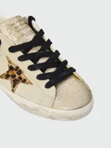 Zapatillas Golden Goose modelo Super Star, color crema con puntera dorada brillante, estrella de animal print y cordones negros.