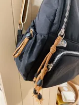 Mochila negra de nylon con grifa bordada, correas combinadas y detalles de cordones.