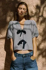Blusa de cuello redondo con escote pico y manga corta abullonada acabada en elástico. Cierre frontal con lazos. Diseño a rayas verticales blancas y negras.