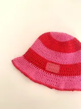 Sombrero tipo bucket tejido a crochet a mano, con hilo 100% algodón y diseño a rayas en tonos rosa y rojo. Presenta una etiqueta con el logo de la marca Cilento en el frente.