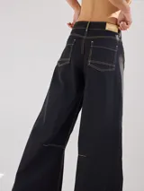 Pantalón ancho negro de algodón y lino con costuras en color mostaza, pinzas debajo de la rodilla y bordado de monograma en el bolsillo delantero.