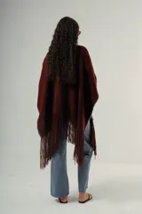 Ruana tejida a mano en lana merino 100%, de color marrón con detalles de costura en rojo en los bordes y terminación de flecos largos en el ruedo. Presenta una silueta amplia y caída natural, confeccionada artesanalmente por Manos del Uruguay.