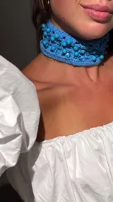 Choker de crochet color celeste tejido a mano con detalles de canutillos y cuentas al tono. Presenta un diseño ancho de estilo artesanal ideal para looks veraniegos.