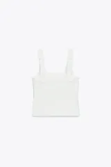 Top blanco de tejido elástico con escote cuadrado y tirantes anchos con lazos decorativos.