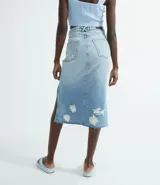 Falda midi de jean celeste con roturas, aberturas laterales y terminación desflecada.
