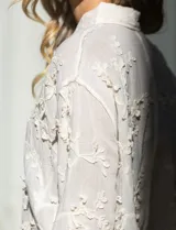 Camisa de algodón color crema, marca Liv Los Angeles, con bordado floral y terminaciones en crochet en puños y ruedo. Tiene cuello con solapa y abertura central con botones.