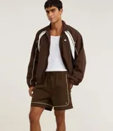 Bermuda deportiva masculina color marrón, con cintura elástica y cordón ajustable. Presenta piping contrastante en blanco a lo largo de los bordes y bolsillos funcionales. Confeccionada en poliamida de secado rápido.