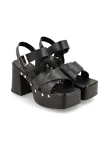 Sandalias negras de plataforma con taco ancho y tiras cruzadas sobre el empeine. Ajuste con hebilla al tobillo y detalle de tachas plateadas en la plataforma.